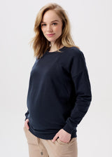 Schwangere Frau trägt dunkelblauen Umstands-Pullover mit zwei seitlichen Reissverschlüssen, welche als Stillfunktion dienen.
