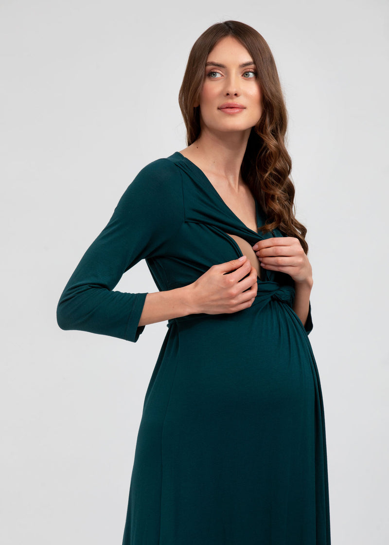 Schwangere Frau trägt enganliegendes Umstands-Strickkleid in Weiss mit grünen Streifen. Das Schwangerschaftskleid ist knielang und kurzärmelig. Es betont den Babybauch