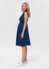 Schwangere Frau trägt blaues, ärmelloseses Jerseykleid in Wickeloptik. Das Kleid eignet sich dank der versteckten Stillfunktion sehr gut zum Stillen.