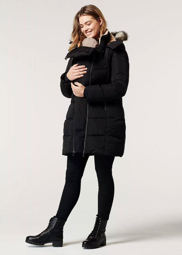 Frau trägt Baby, sie hat die Umstands-/Tragejacke in Schwarz von Noppies.