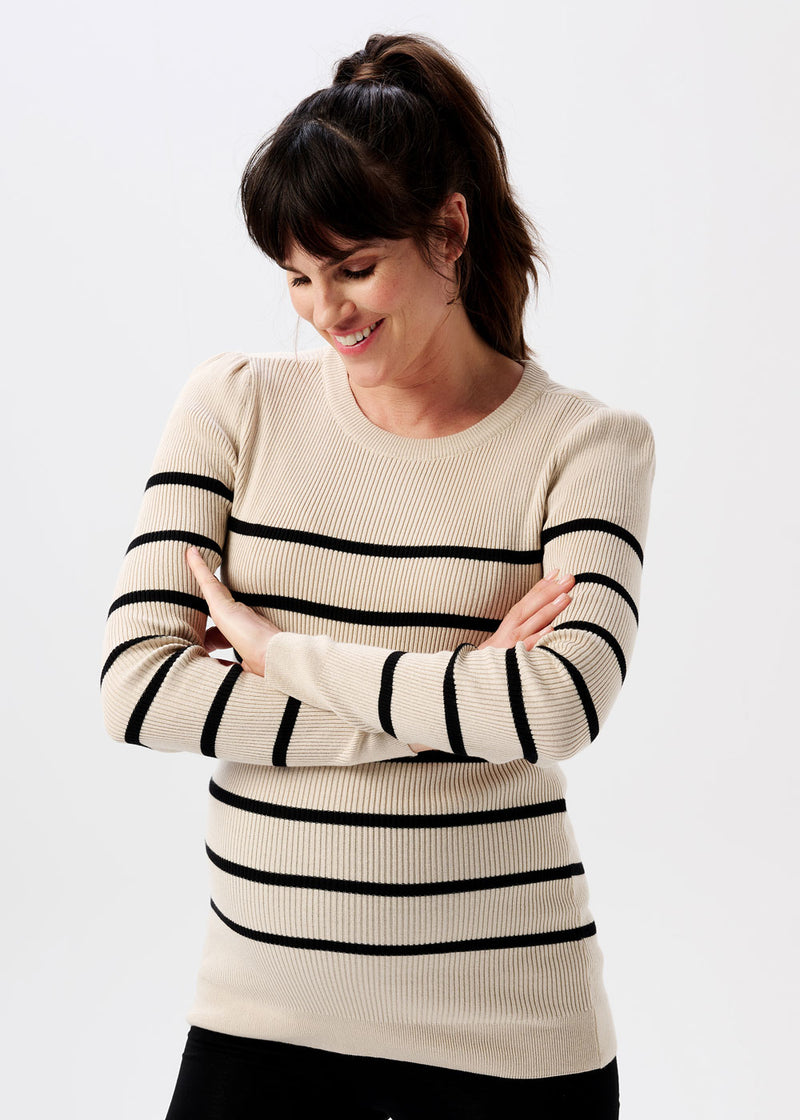 Schwangere Frau trägt beigefarbenen Umstands-Strickpullover mit kleinen Puffärmeln und schwarzen Streifen.