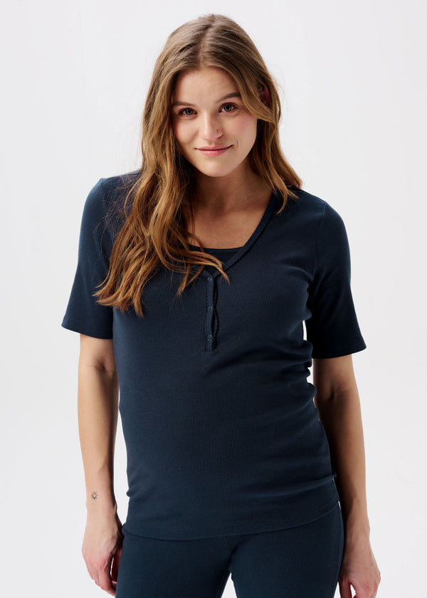 Schwangere Frau trägt kurzärmeliges Shirt in Dunkelblau. Das Shirt hat vorne Knöpfe, welche das Stillen erleichtern.