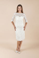 Das Model trägt das kurze Umstands-Hochzeitskleid Alessia in Weiss. Das Kleid ist figurnah geschnitten und wirkt durch die florale Spitze und die 3/4-Ärmel elegant und feminin. Ein stilvoller Look für Ziviltrauung/Standesamt und andere festliche Anlässe in der Schwangerschaft.