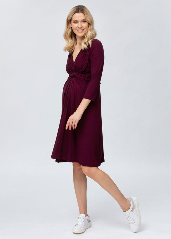 Junge Frau trägt bordeaufarbenes Schwangerschafts-Kleid in Wickeloptik mit langen Ärmeln. Das Kleid verfügt über eine versteckte Stillfunktion