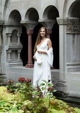 Schwangere Frau trägt bodenlanges Umstands-Brautkleid mit perlenbesetztem Spitzenoberteil.