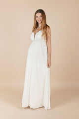 Das Model trägt das lange Umstands-Hochzeitskleid Mara in Weiss. Der tiefe V-Ausschnitt mit transparentem Einsatz wirkt modern und elegant, während der fliessende, lange Rock dem Babybauch angenehm Platz gibt und wunderschön fällt – ideal für Standesamt/Ziviltrauung oder eine festliche Trauung.