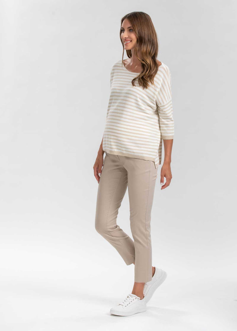 Schwangere Frau trägt beige, eng geschnittene Umstands-Business-Hosen in 7/8-Länge.
