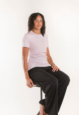 Model sitzt auf Hocker und trägt Still-T-Shirt Essential in Pastellrosa mit diskreter Stillfunktion.