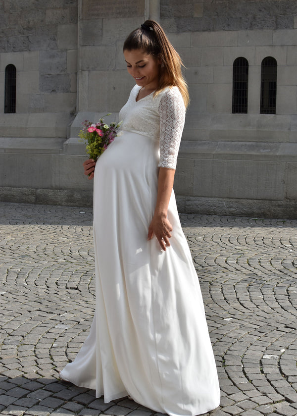 Schwangere Frau trägt ein bodenlanges Umstands-Brautkleid mit V-Ausschnitt und Dreiviertel-Ärmeln