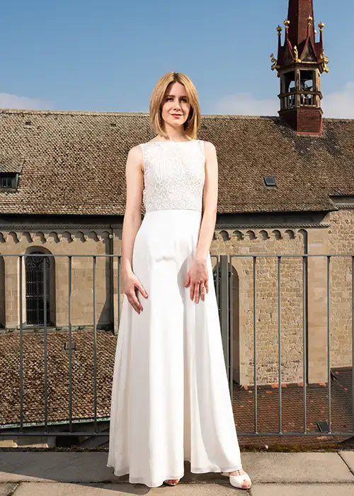 Schlenke Frau trägt langes Hochzeitskleid mit Spitzen-Cutout-Rücken. Das elegante und schmal geschnittene Kleid eignet sich für Standesamt und Kirche. Im Hintergrund sieht man das Grossmünster.