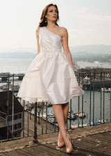 Frau trägt elegantes One-Shoulder-Kleid aus ecrufarbener Wildseide. Im Hintergrund sieht man den Zürichsee. Das Kleid eignet sich für die Ziviltrauung.