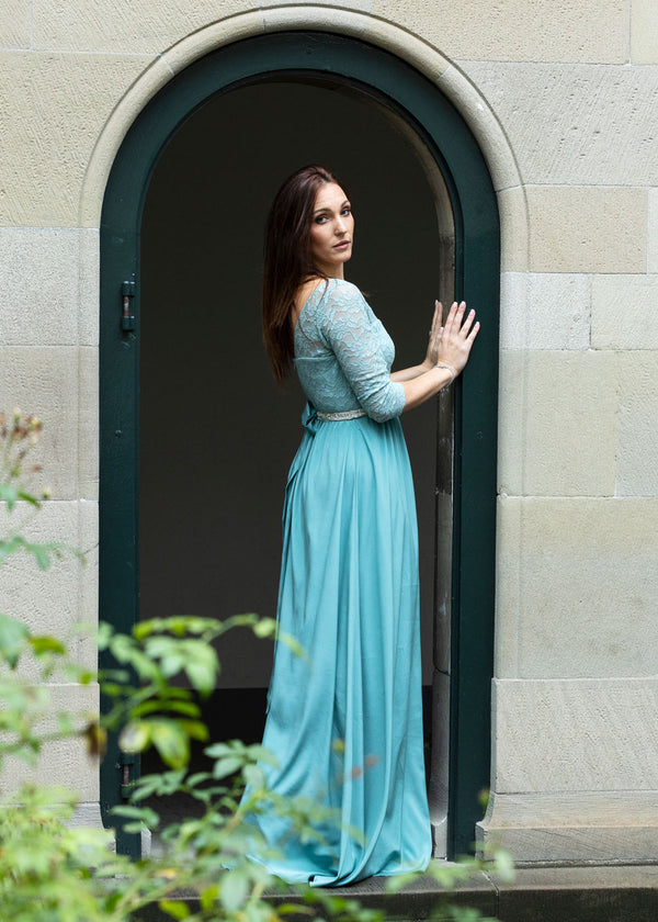 Frau trägt festliches bodenlanges Seidenkleid in Aqua mit Spitzenoberteil und Dreiviertel-Ärmeln
