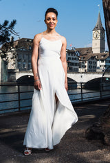 Schlanke Frau trägt Seiden-Hochzeitskleid mit Spaghettiträgern. Der Rock ist bodenlang, vorne aber offen, so dass man die Beine sieht. Im Hintergrund ist die Limmat mit dem Fraumünster.